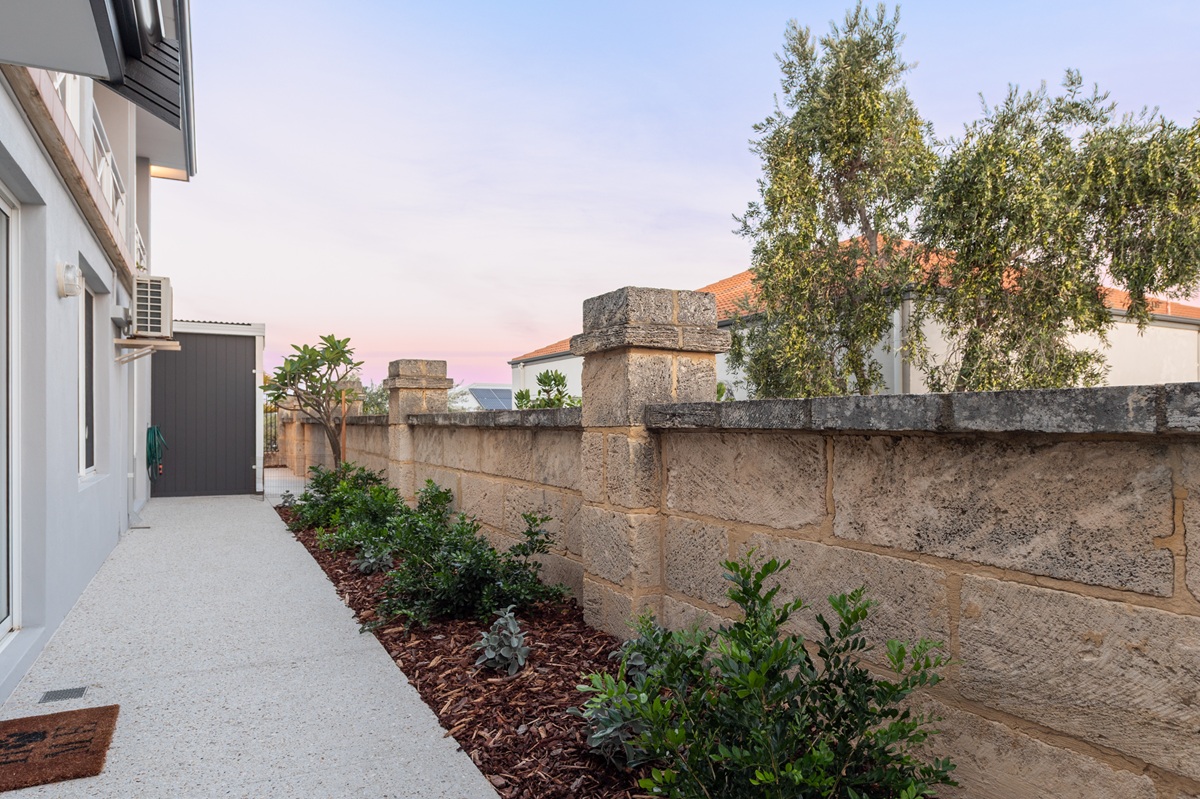 Natural limestone retaining wall with capped piers bordering a mulched garden bed.