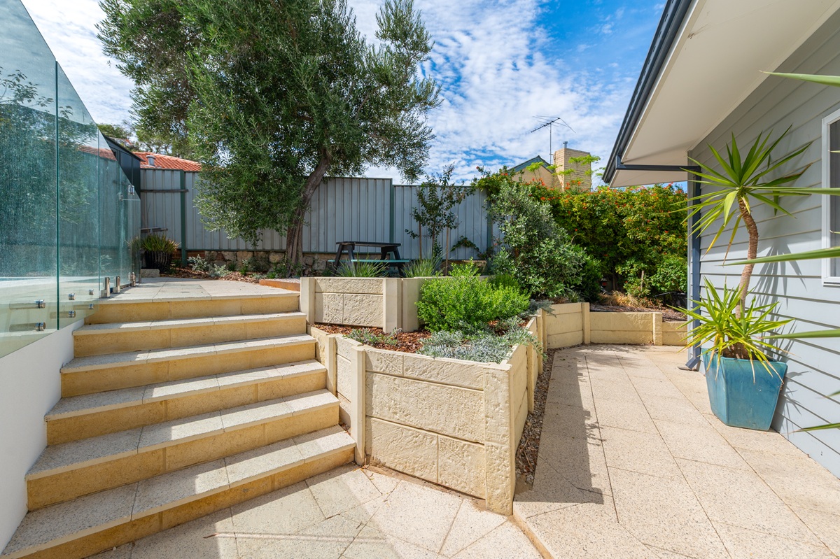four main retaining wall materials comparison Tiered stone-look block retaining walls forming garden planters beside matching paved steps.