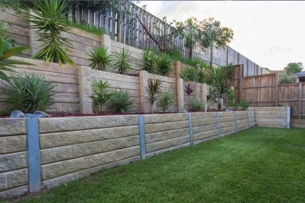 A multi-tiered concrete sleeper retaining wall supported by steel posts, managing a steep slope in a residential backyard.